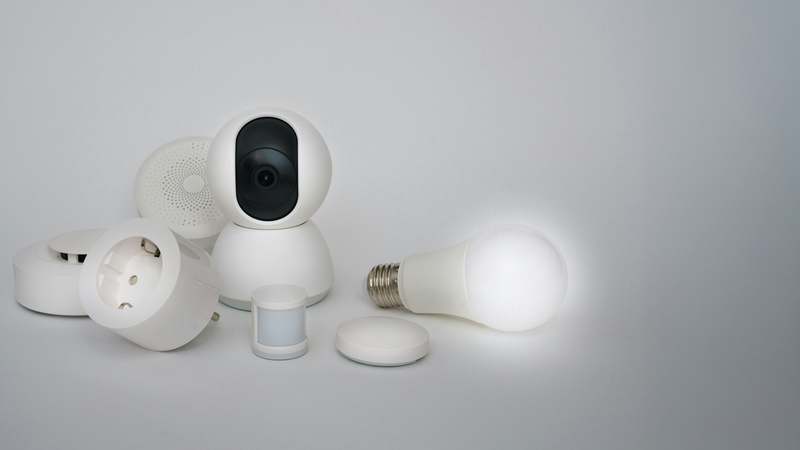 Overhead shot of a smart home security camera setup: indoor cam on shelf, outdoor cam on eaves, smartphone displaying app interface with motion alerts